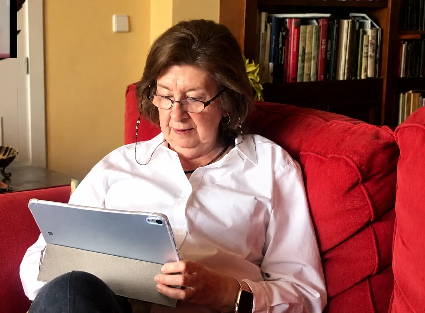 Señora mayor entrenando con una tableta en el sofá de su casa